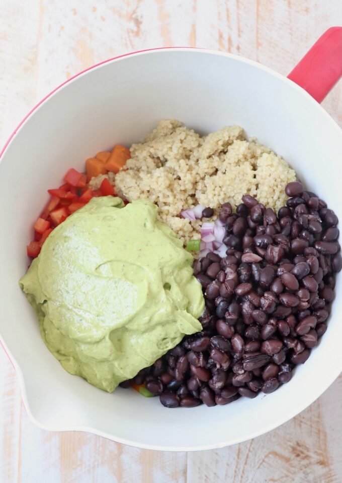 black beans, quinoa and diced vegetables in mixing bowl with avocado salad dressing