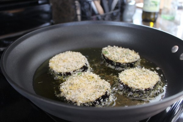 Coated eggplant slices cooking in a pan with oil. 