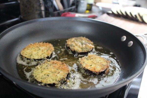 Slices of eggplant coated in breadcrumbs cooking in a pan with oil. 