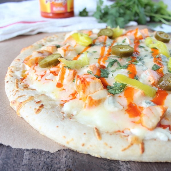 Pizza topped with melted cheese, chicken, buffalo sauce, pepperoncinis, and jalapeños.