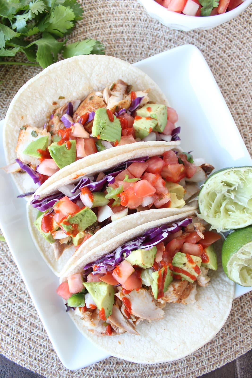 fish tacos on white plate, topped with diced avocado and hot sauce