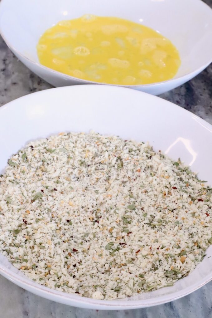 bowl of seasoned breadcrumbs next to a bowl with a whisked egg