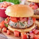 Turkey burger on bun on wood cutting board topped with diced tomatoes