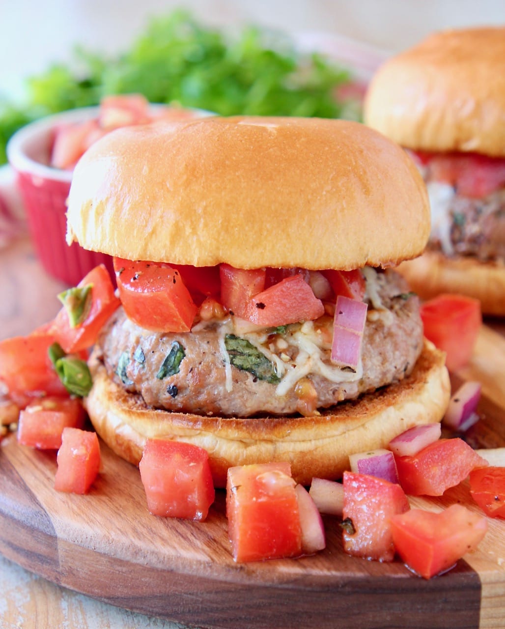 Turkey burger on bun on wood cutting board topped with diced tomato bruschetta