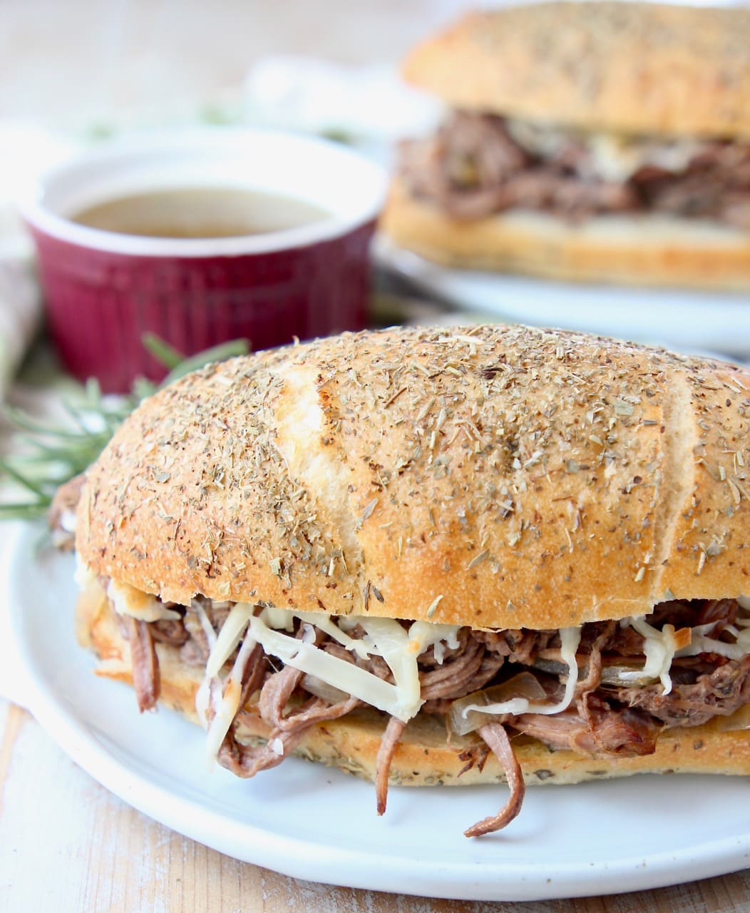 Shredded tri tip sandwich on plate with bowl of au jus
