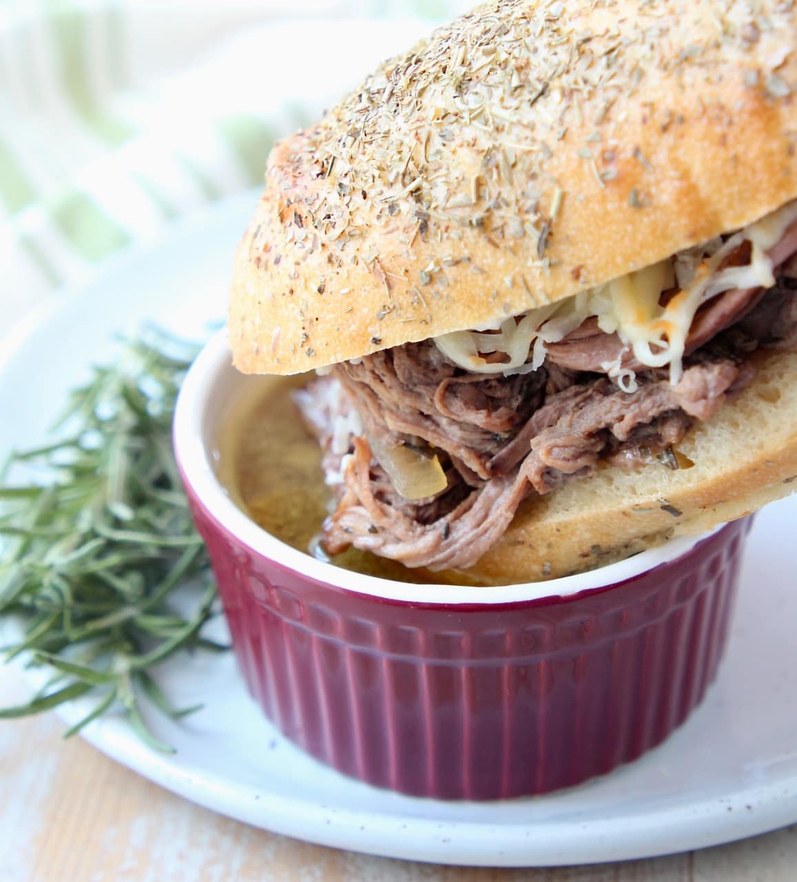 Tri Tip French Dip Sandwich being dipped into a bowl of au jus