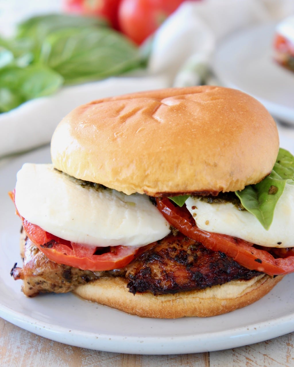 Grilled chicken sandwich with tomatoes, basil and mozzarella cheese on white plate