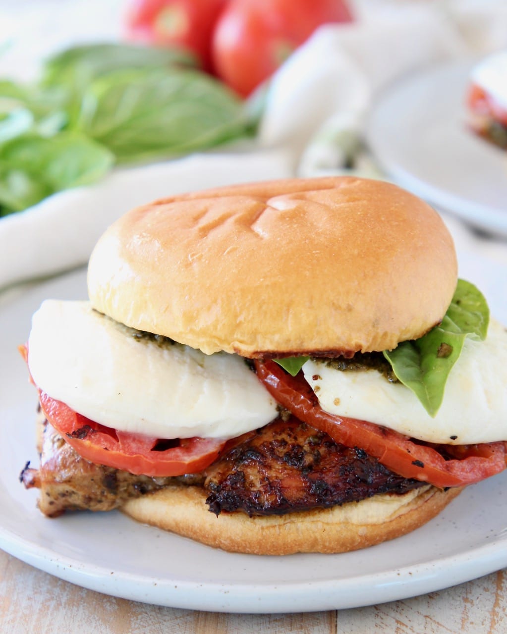 Grilled chicken sandwich with tomatoes and mozzarella cheese on white plate