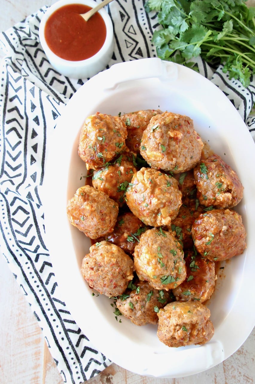 Taco meatballs in bowl with side bowl filled with hot sauce on black and white printed towel