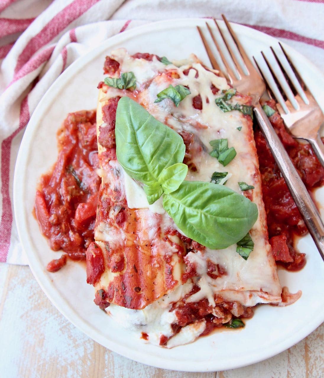 Manicotti on plate with fresh basil leaves and copper forks
