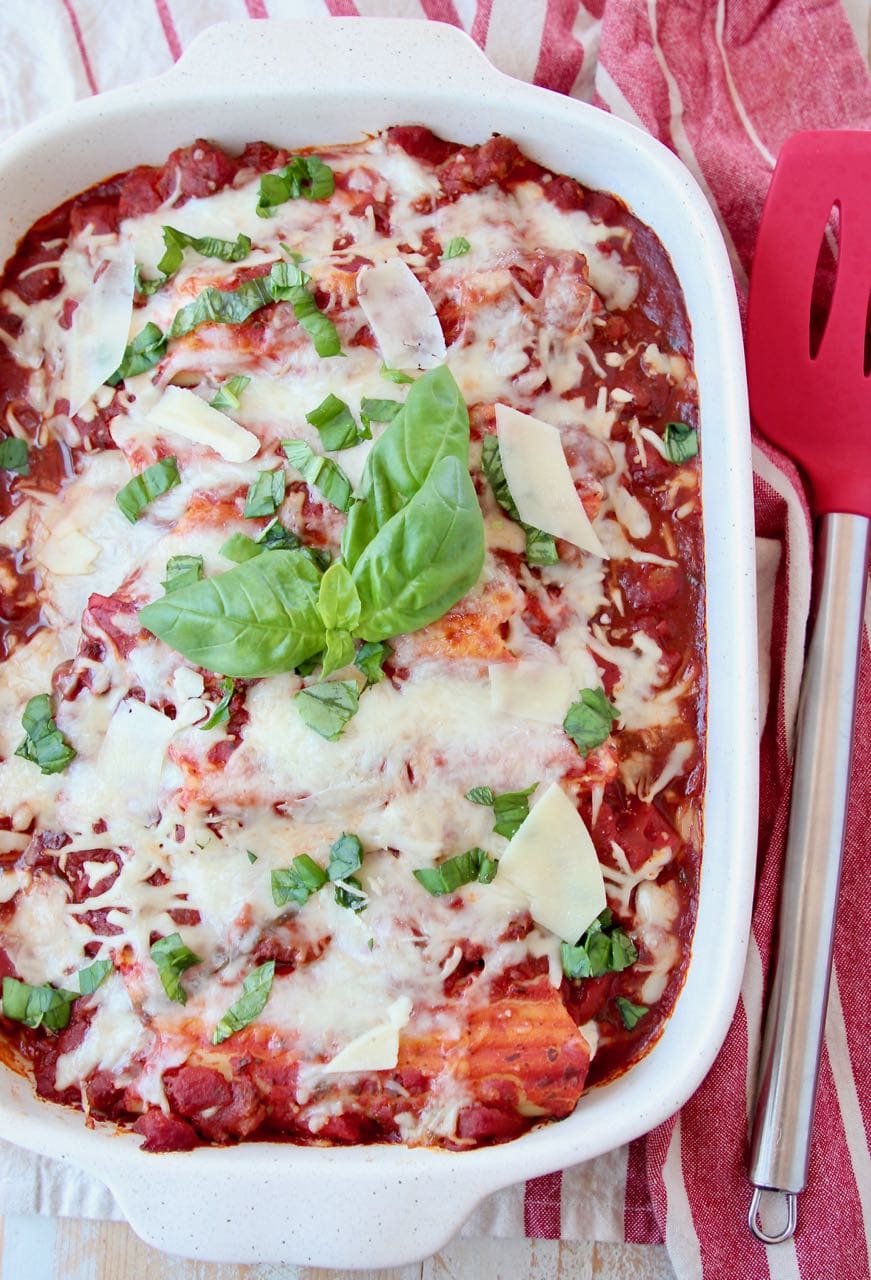 Baked manicotti in casserole dish topped with fresh basil leaves