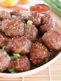 Chinese orange glazed meatballs in bowl with sesame seeds and green onions on top