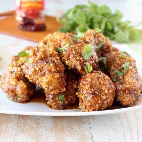 baked breaded boneless wings tossed in sauce on a white plate