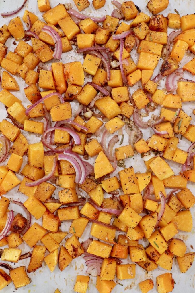 roasted cubed butternut squash with sliced onions and minced garlic on a parchment paper lined baking sheet