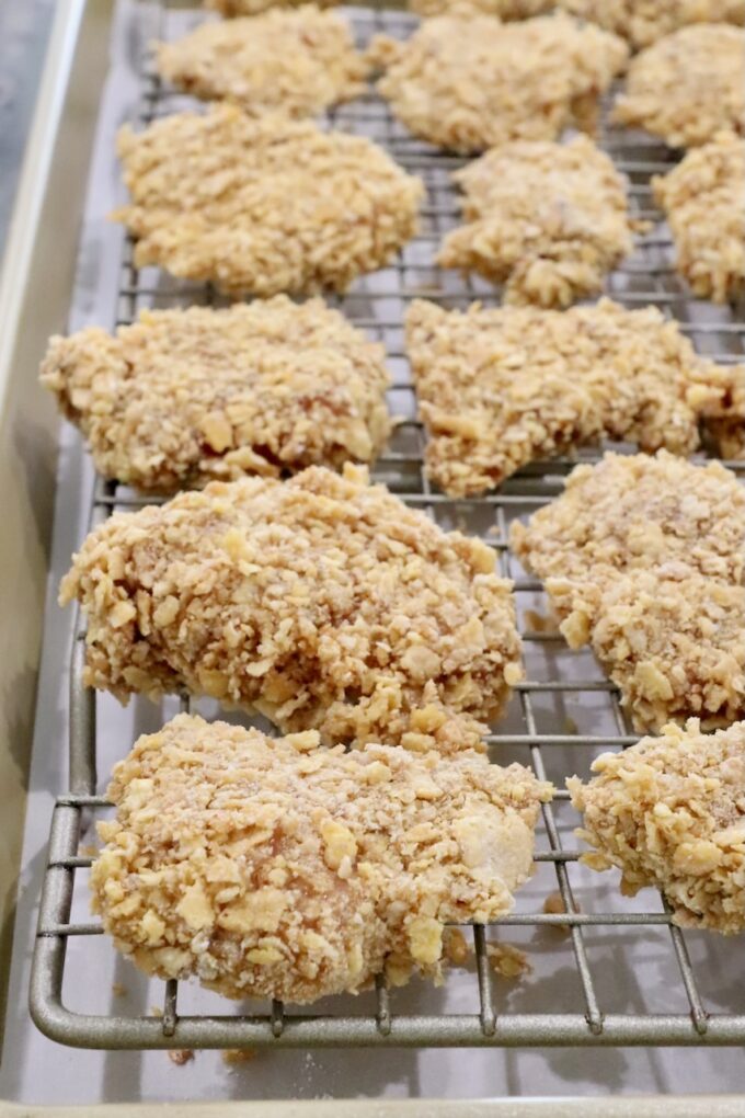uncooked breaded pieces of chicken on a wire rack on top of a baking sheet