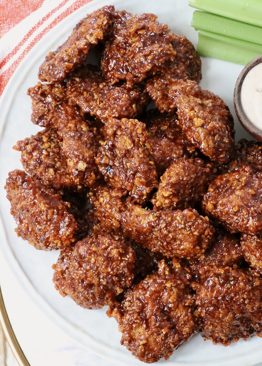 cooked, breaded chicken crispers, tossed in sauce, stacked up on a plate