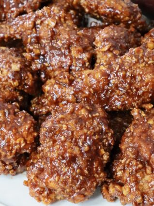 cooked chicken crispers tossed in sauce stacked up on a plate