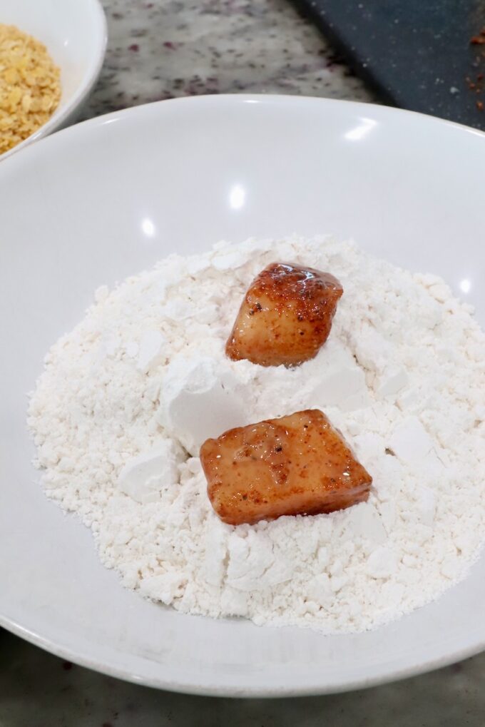 seasoned raw pieces of chicken in a bowl of flour