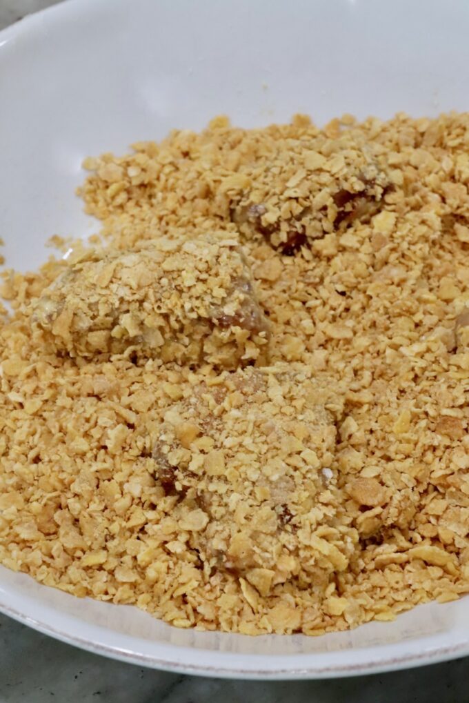 breaded pieces of chicken in a bowl of crushed corn flakes