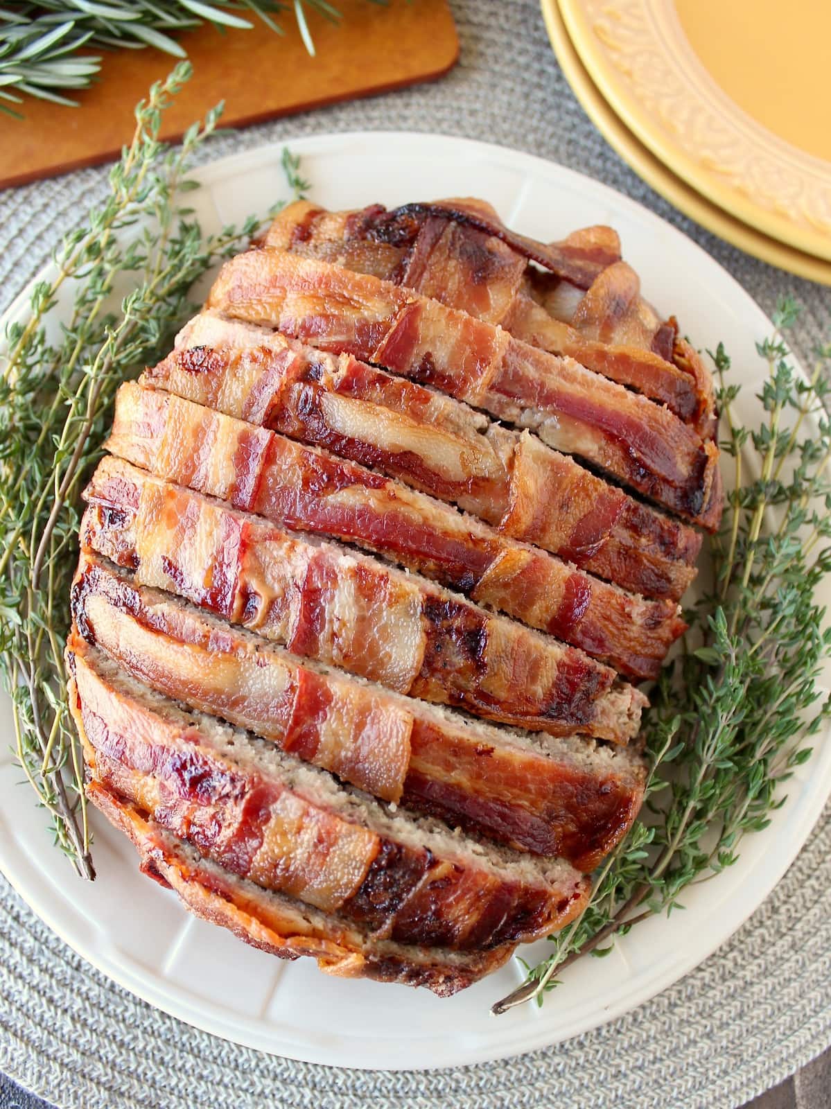 Sliced bacon wrapped meatloaf on plate with fresh herbs