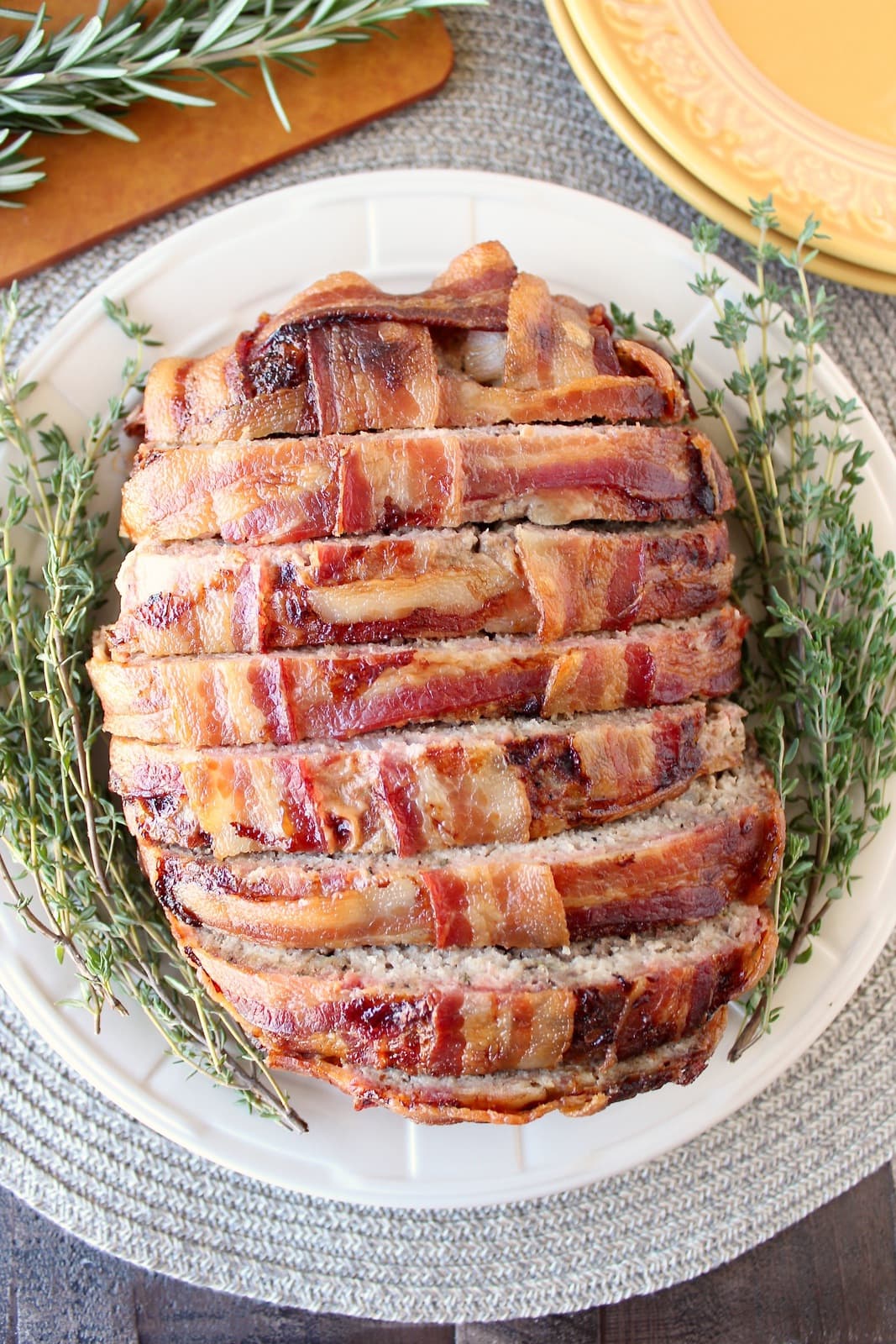overhead image of sliced Bacon Wrapped Meatloaf on plate with fresh thyme sprigs