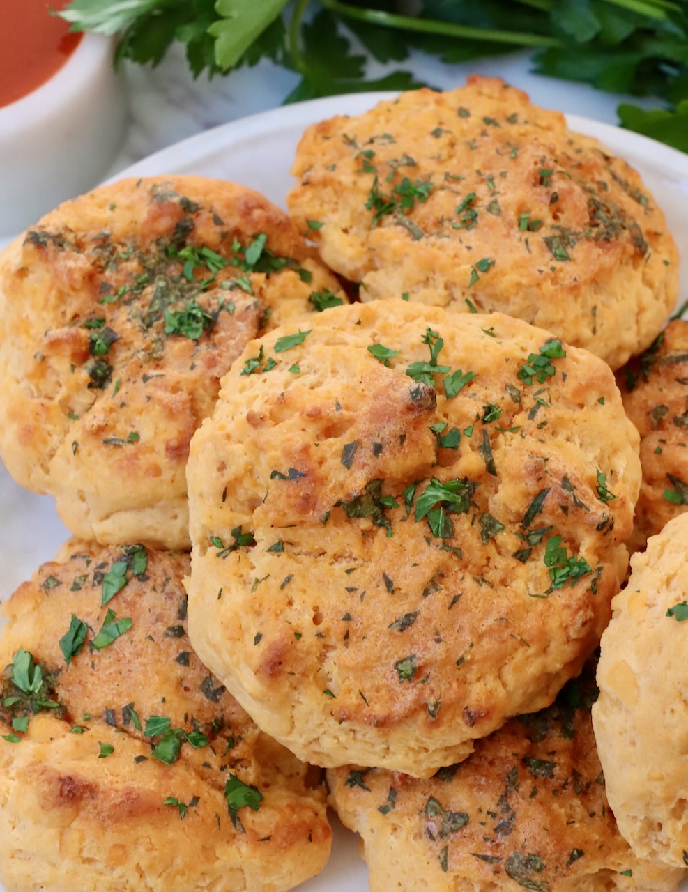 cheddar biscuits stacked up on a plate topped with fresh chopped parsley
