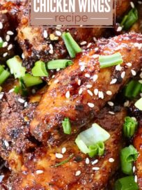 cooked chicken wings tossed in sauce piled up on a plate, topped with diced green onions and sesame seeds