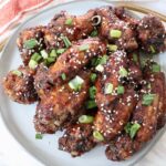 cooked chicken wings tossed in sauce and piled up on a plate with diced green onions and sesame seeds
