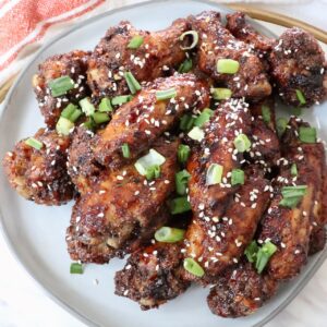 cooked chicken wings tossed in sauce and piled up on a plate with diced green onions and sesame seeds