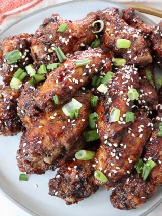 cooked chicken wings tossed in sauce and piled up on a plate with diced green onions and sesame seeds