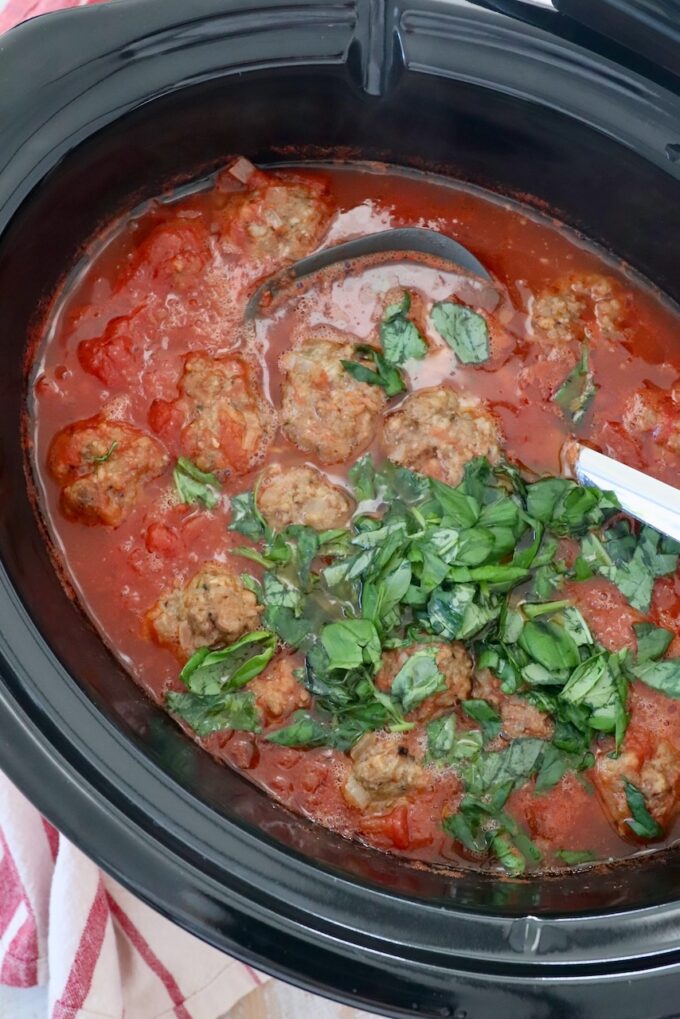 meatballs in slow cooker with tomato sauce, fresh basil and serving spoon