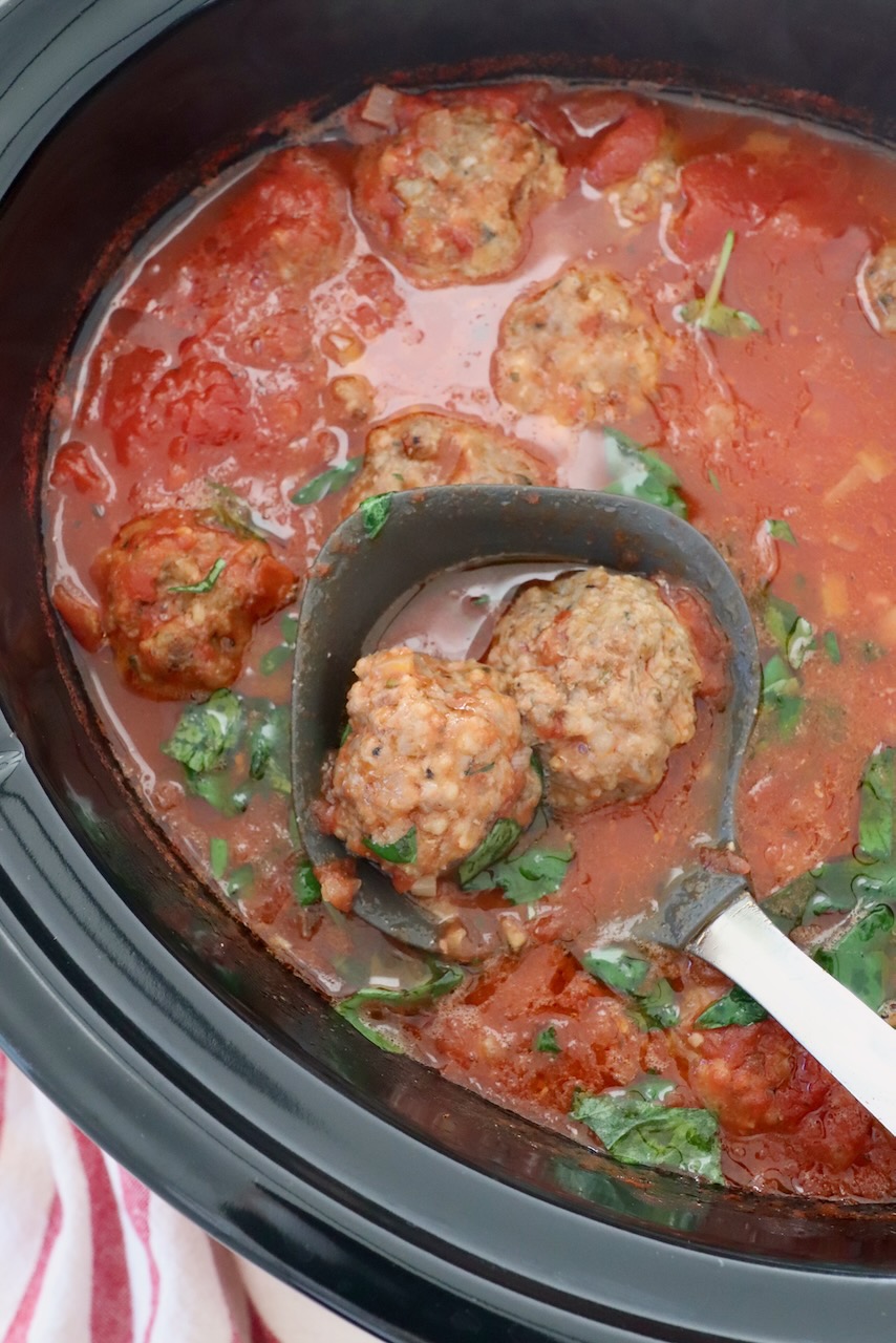 cooked meatballs in tomato sauce with serving spoon in a slow cooker