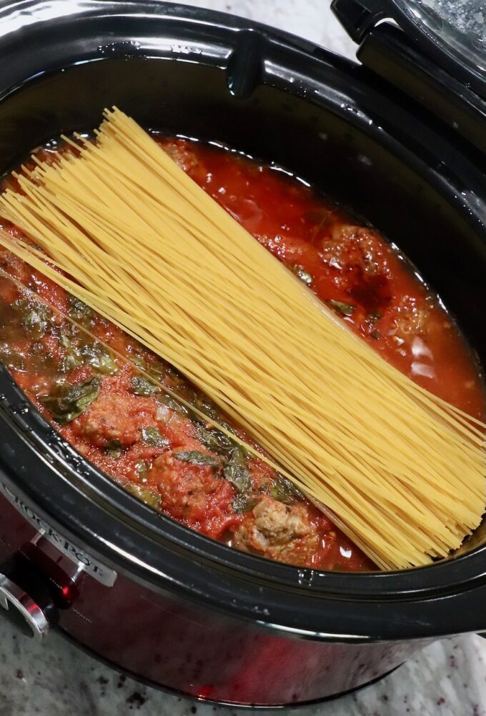 uncooked spaghetti noodles in slow cooker with Italian meatballs and marinara sauce