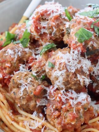 cooked meatballs on top of spaghetti and tomato sauce in bowl with fork