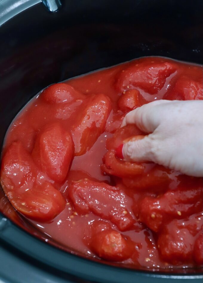 hand reaching into slow cooker filled with whole canned tomatoes