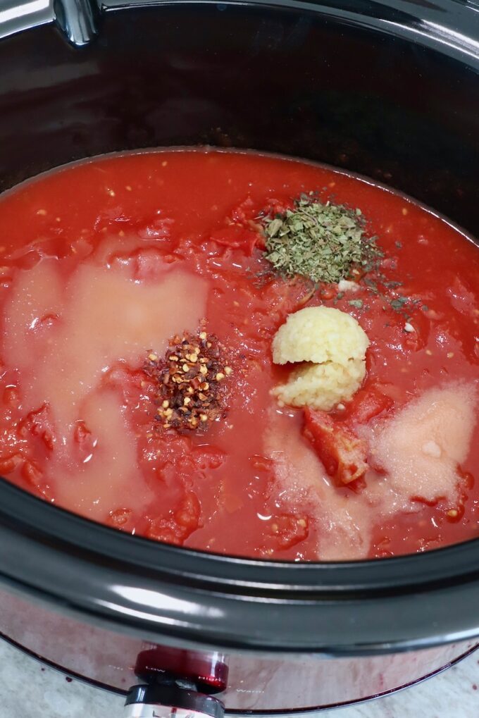 tomato sauce in slow cooker topped with spices and herbs