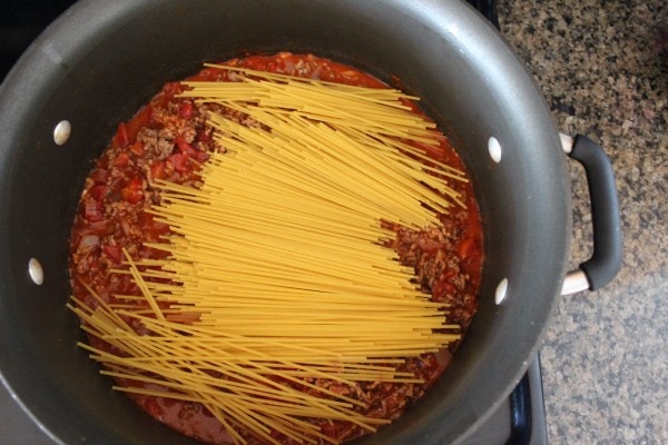 Uncooked spaghetti noodles on top of meat and red sauce in a pan.