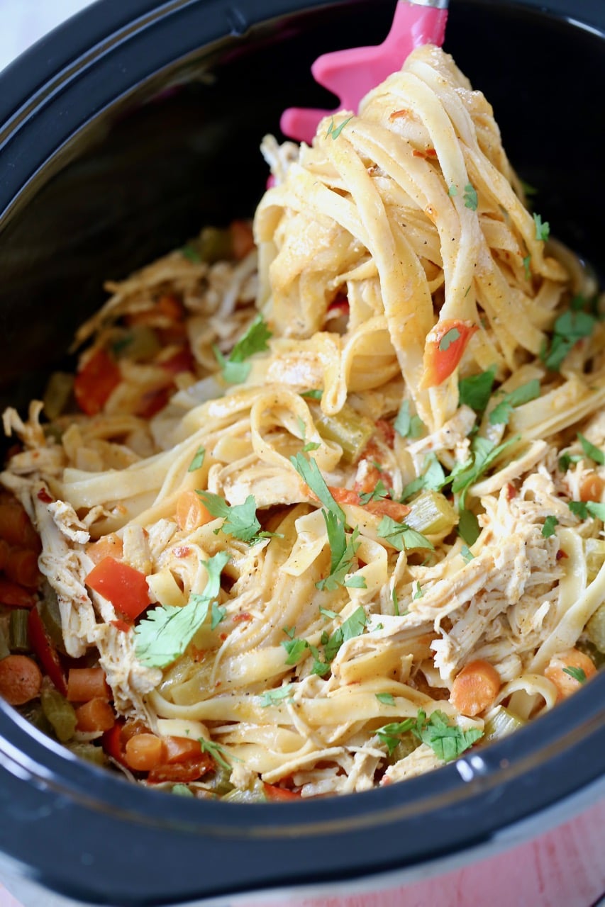 Buffalo chicken alfredo pasta in a crock pot with a spoon scooping the pasta out of the crock pot