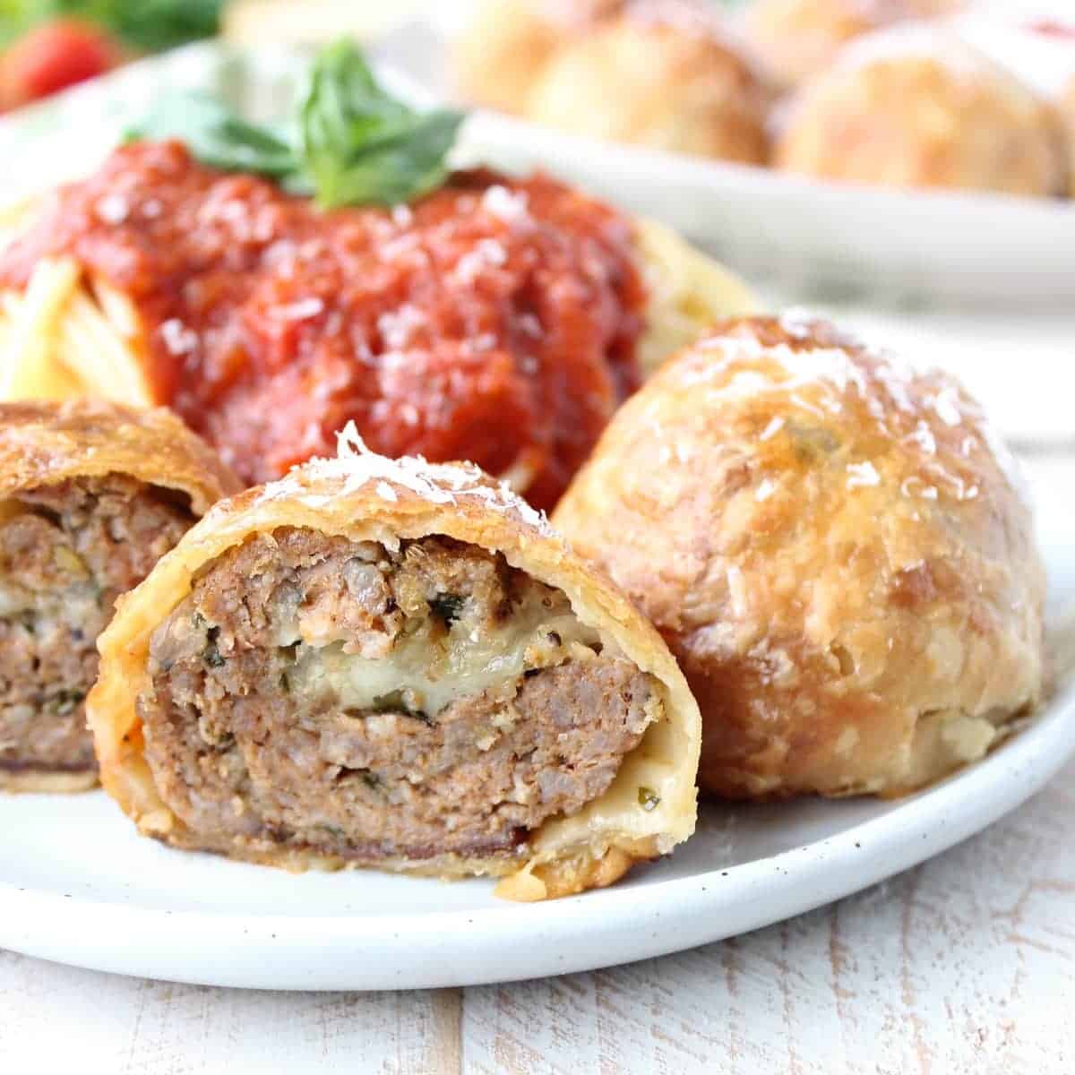 baked puff pastry wrapped meatball cut in half on plate with spaghetti and red sauce