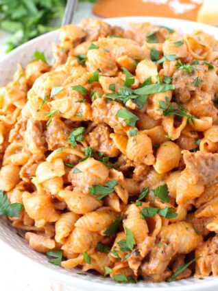A close-up of creamy pasta shells mixed with a savory sauce and ground meat, garnished with fresh parsley.