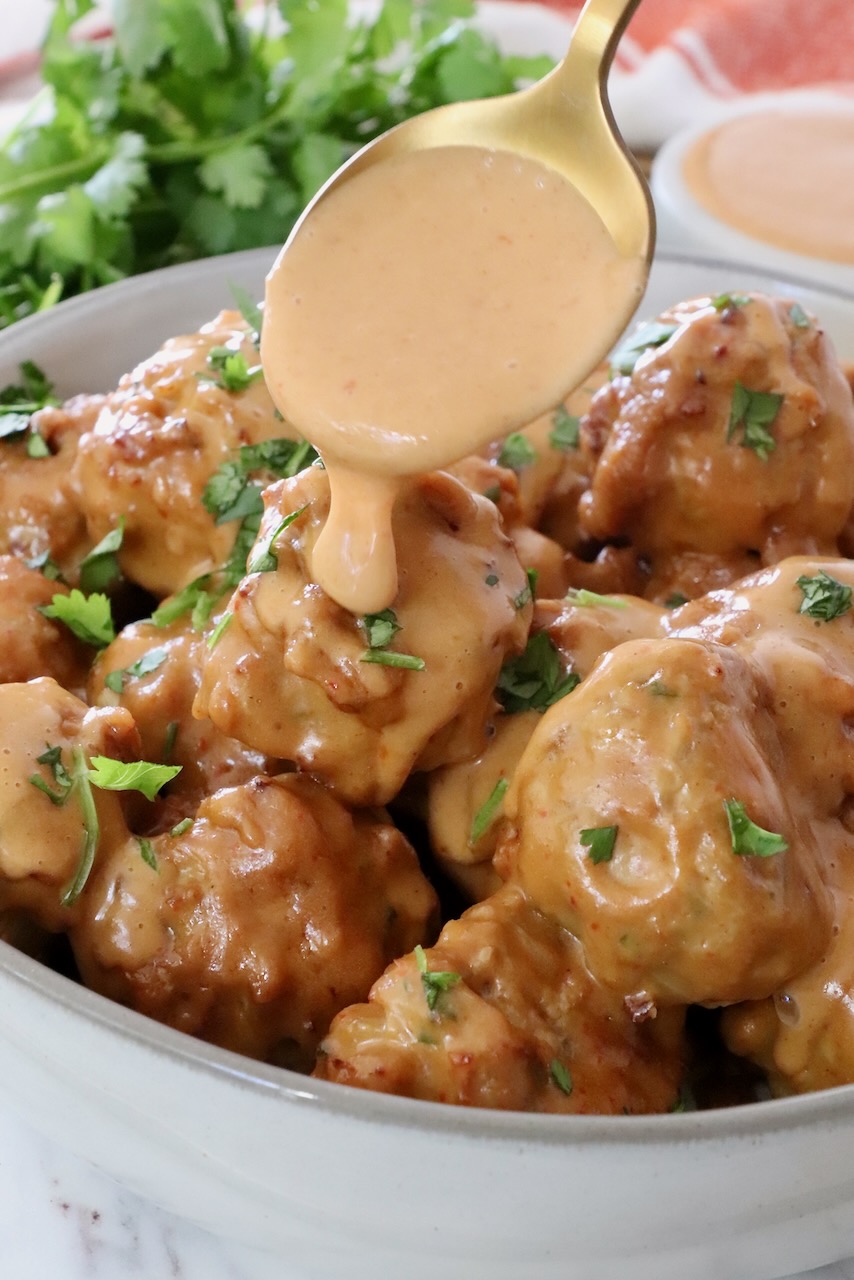 meatballs in bowl with spoon of peanut sauce drizzling over the meatballs