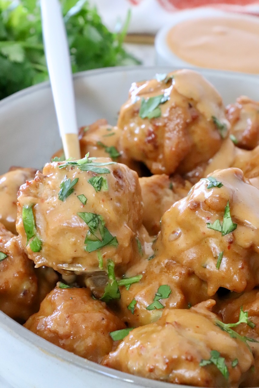 meatballs in bowl with spoon, covered in peanut sauce