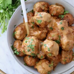 meatballs covered in peanut sauce in a bowl with a spoon