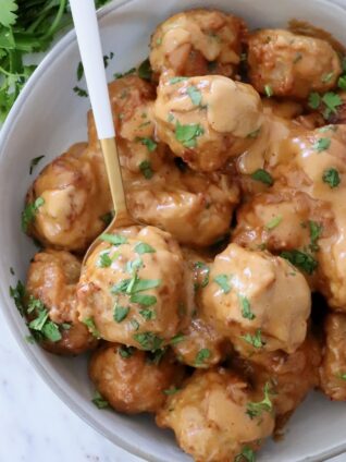 meatballs covered in peanut sauce in a bowl with a spoon