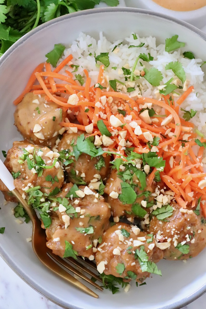 meatballs covered in peanut sauce in a bowl with rice and carrots