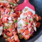 cooked chicken topped with tomato bruschetta in a skillet with a red spatula