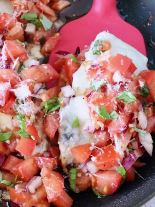 cooked chicken topped with tomato bruschetta in a skillet with a red spatula