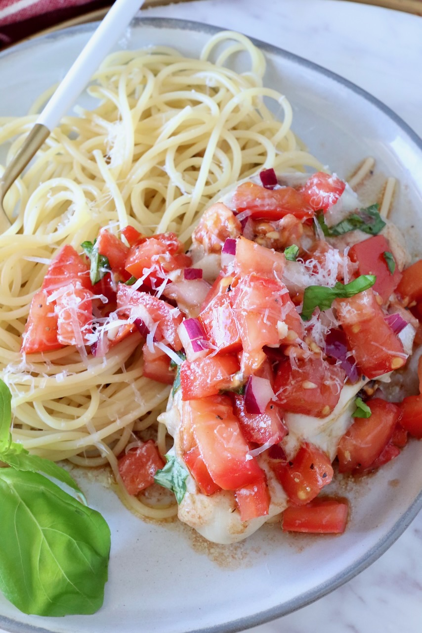 chicken topped with tomato bruschetta on a plate with cooked spaghetti noodles