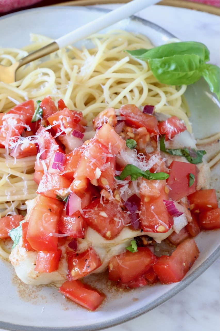 cooked chicken on a plate next to spaghetti noodles covered with tomato bruschetta