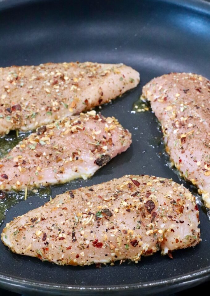 raw seasoned chicken breasts in a skillet